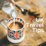 Image of tea cup decorated with a British flag having milk being poured into the tea with cookies/biscuits in the background with text overlay 7 UK travel tips to know before you go.