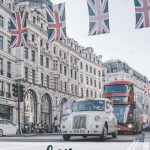 White classic car and red, double decker bus on London street with british flags. London With Kids: Transport, Eats & Sleeps. Everything you need to know to plan affordable travel in London with kids.